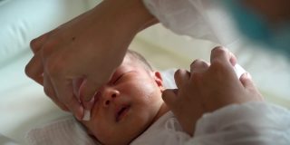 婴儿护理员用湿棉球清洁新生儿面部