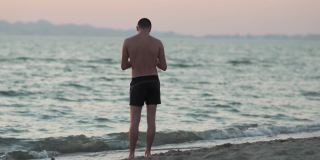 年轻男子在热带海滩上用手机拍摄令人惊叹的夏日日落、日出。慢动作