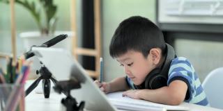 小男孩在家里用互联网交流。家庭教育，远程教育，亚洲小男孩在网上上课，为家庭学校隔离感到高兴。