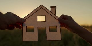 夕阳西下，家家户户拥着纸屋，阳光透过窗户照进来。手握剪纸的房子符号在日落