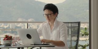 短发女性在度假期间在户外露台上用笔记本电脑远程工作。Rbbro成年女性