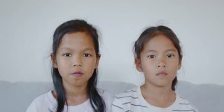 两个亚洲小女孩的肖像看着相机，微笑着，在客厅幸福地一起笑。慢动作50 FPS。
