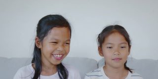 两个亚洲小女孩的肖像看着相机，微笑着，在客厅幸福地一起笑。慢动作50 FPS。