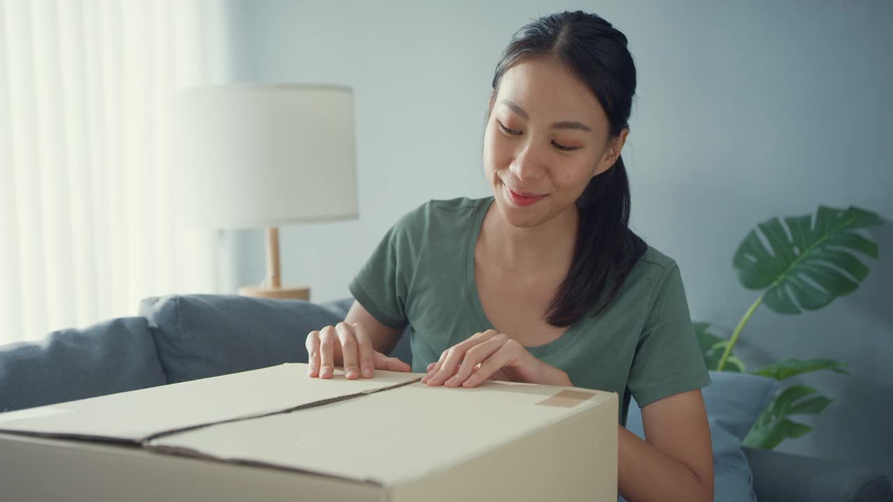 快乐亚洲女士打开纸板箱包装，享受在家中客厅尝试和搭配网上市场的时尚布艺产品。