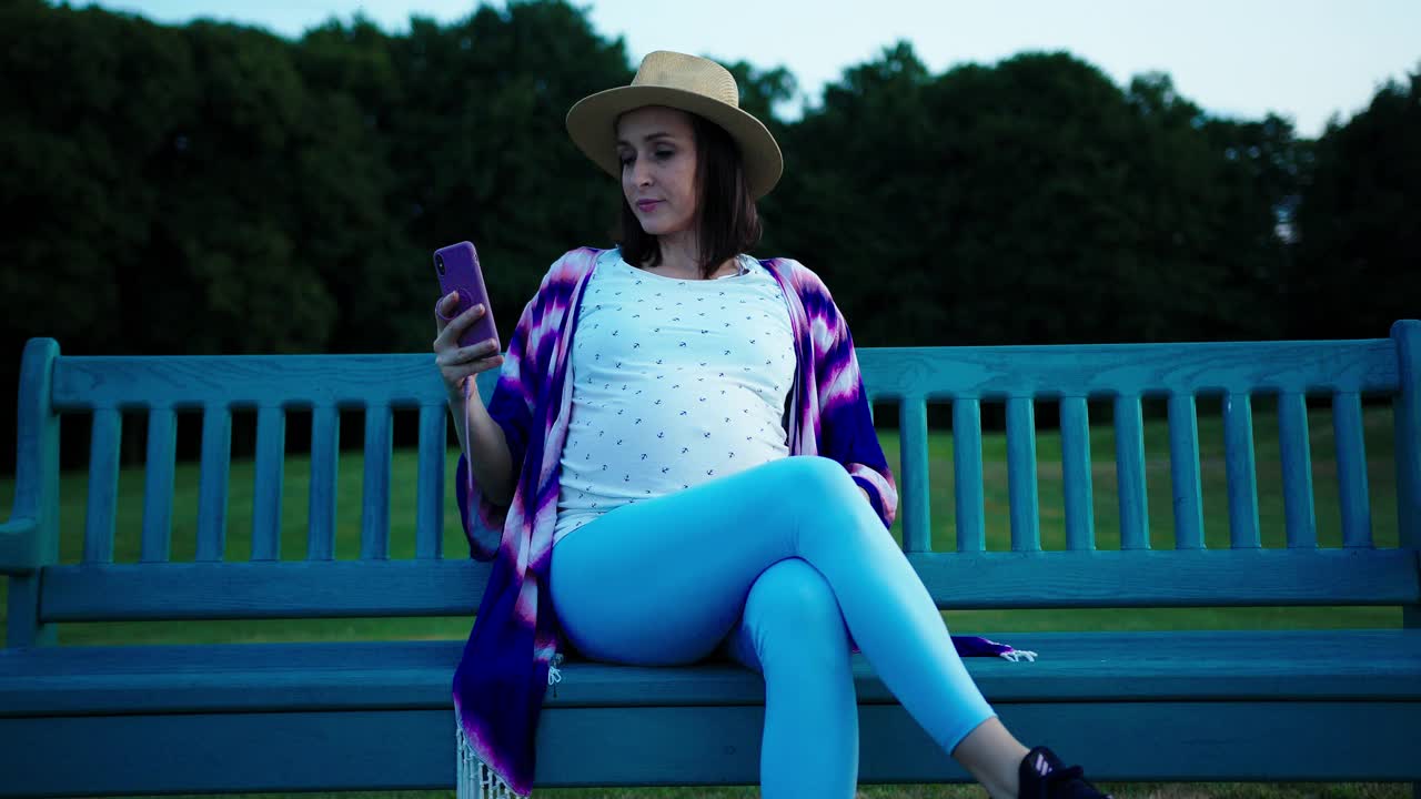 一名白人孕妇戴着帽子在公园里玩手机