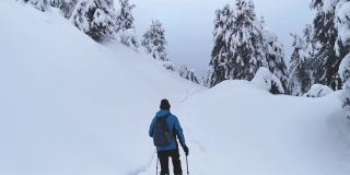 一名游客穿着夹克，穿着雪鞋，拄着拐杖，沿着小路进行冬季徒步旅行。