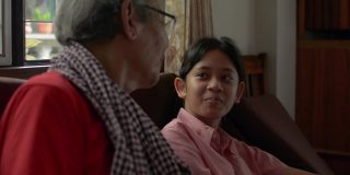可爱的亚洲少女孙女在客厅里和她白发苍苍的爷爷坐在一起聊天，开心地笑着。家庭中两代人的联系。
