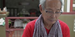 亚洲的老爷爷穿着便装在家里和朋友在智能手机上聊天，他可爱的孙女过来在他耳边兴奋地低语。