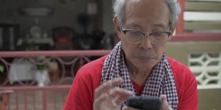 当她的祖父在家里使用手机时，一个亚洲可爱的孙女走近他，兴奋地在他耳边低语。家庭中两代人的联系。