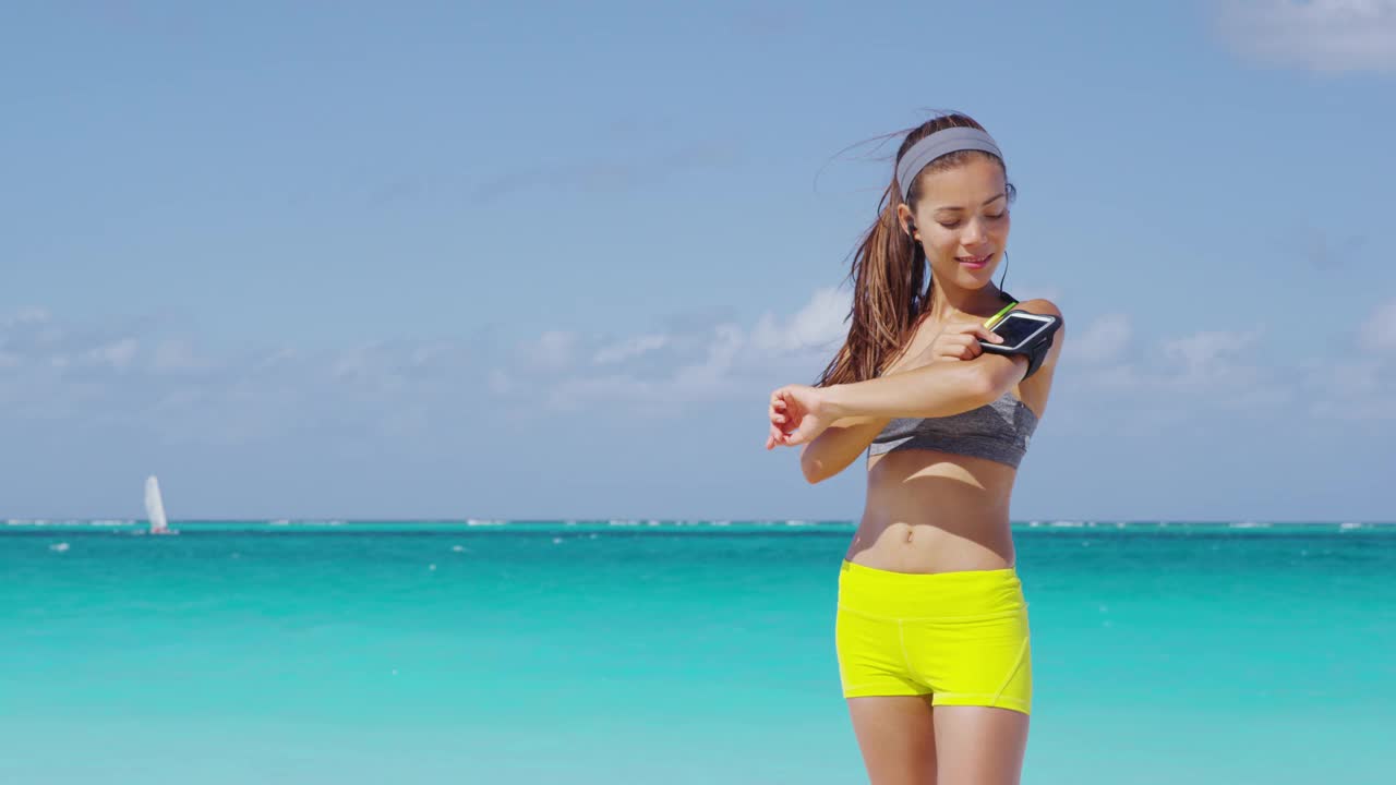 健身女性在臂章上使用智能手机健身应用。年轻的亚洲女跑步运动员用手机触摸运动臂带上的触摸屏，听音乐或作为运动追踪器。