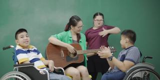 组亚洲残疾儿童在轮椅和自闭症演唱活动老师在教室弹吉他。提高学习技能的活动。贫困儿童教育