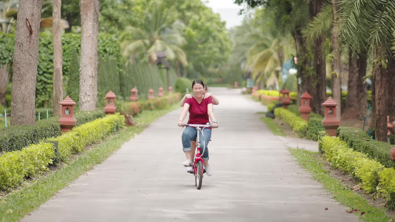 快乐的亚洲女孩和她的妈妈在公园里骑自行车