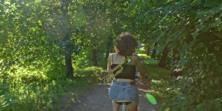 一位女艺术家在阳光下骑着自行车穿过绿色的小巷，享受生活