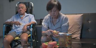 亚洲华人老夫妇坐在轮椅上享受电影之夜，坐在客厅的沙发上看电视