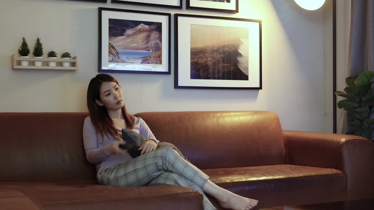 亚洲妇女坐在家里的沙发上看电视电影。