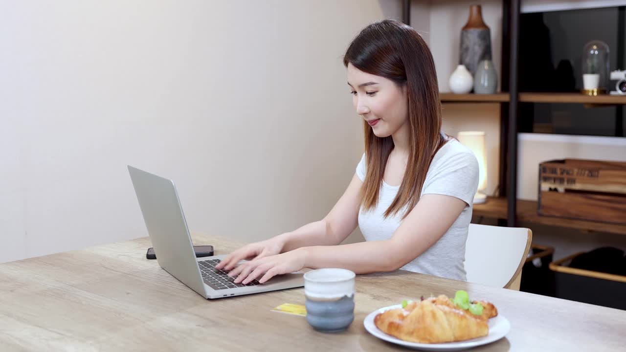 漂亮的女人在家里用笔记本电脑工作，亚洲女商人在家里通过视频在线会议。