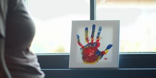 母亲看着孩子的彩色手掌画。记忆和归属感。在她早上上班前的例行公事。