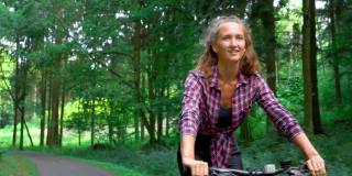 女运动员骑着自行车沿着森林公路，享受空气和风景。