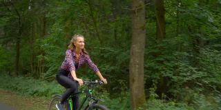 女运动员骑着自行车沿着森林公路，享受空气和风景。