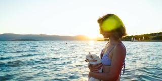 身着比基尼的美女带着一只shiwawa狗在热带海滩上享受着美丽的海景。