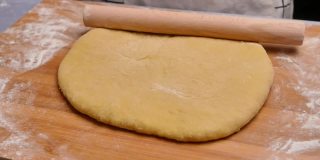 女人们用手在木桌上用擀面杖擀面，准备做披萨或甜甜圈。烹饪过程。