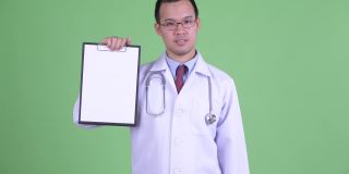 亚洲男人医生的工作室肖像看起来悲伤和拇指向下，而持剪贴板与复制空间在绿色背景