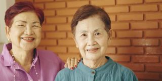 两位亚洲(泰国和中国)姐姐的脸聚焦在一起，在砖墙背景上微笑，表达了她对幸福健康的退休家庭的积极和享受。