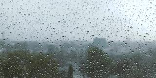 雨点在窗户上的缓慢运动与模糊的背景，雨天，玻璃上的水滴，感觉孤独和悲伤的概念。坏天气的一天。透过窗户看风景