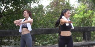 一组两个朋友适合亚洲女性穿着运动服与毛巾伸展和冷却后，锻炼或跑步一起在公园户外。健康的女人在早上为运动训练热身