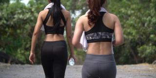 一组两个朋友适合亚洲妇女穿着运动服与毛巾交谈和散步后，锻炼锻炼或慢跑一起在公园户外。健身慢跑的女人在早上进行运动训练