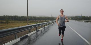 运动员在雷雨中沿着高速公路快速奔跑，正面视图。运动员冒雨在公路上跑马拉松。短跑运动员在锻炼