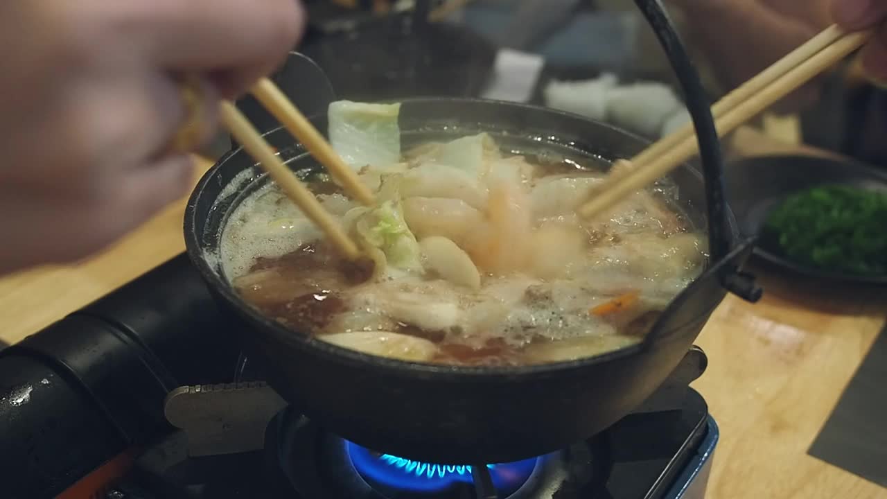 在一家日本餐馆里，餐桌上的每个人都用筷子从涮锅里拿食物。