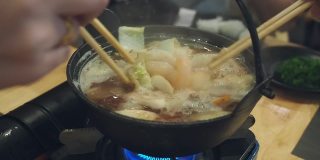 在一家日本餐馆里，餐桌上的每个人都用筷子从涮锅里拿食物。