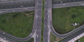 放大高度发达城市中现代三叶草形状的多级沥青交通枢纽的无人机航拍。高架道路和运动车辆的运动，高速公路之间的花坛。