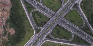 放大高度发达城市中现代三叶草形状的多级沥青交通枢纽的无人机航拍。高架道路和运动车辆的运动，高速公路之间的花坛。