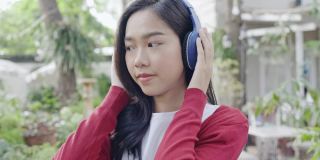 漂亮脸蛋的亚洲少女戴着耳机蓝色快乐的音乐在夏季公园在家里。女士度假旅行。女孩自信的微笑让你在家的时候感到放松。概念积极的态度
