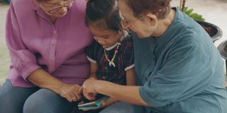 两位亚洲(泰国、中国)老奶奶和孙女一起玩智能手机，玩得很开心，体现了现代生活中利用互联网技术与人交流的理念。