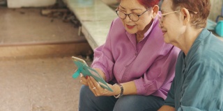 近4K的坐着两个亚洲老年姐妹玩智能手机的乐趣和享受，展示了婴儿潮一代利用互联网技术与现代生活中的人联系的概念。