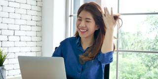 幸福亚洲女人在家工作使用笔记本电脑在线会议在家庭办公室。快乐放松时间亚洲商业女性打字键盘使用笔记本电脑笔记本电脑微笑，大笑在家里办公室。