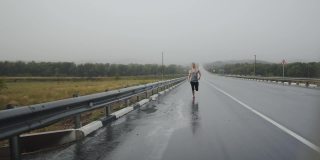 运动员在雨中跑马拉松的路上渐渐远去，眼前的景象。运动员在雷雨中沿着公路奔跑