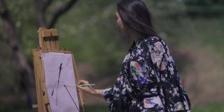 年轻自信的亚洲美女穿着和服在帆布上作画，在春天阳光明媚的公园户外。灵感迸发的天才日本画家在阳光下的侧视中景。技巧和灵感。