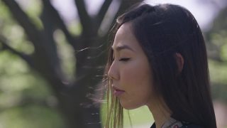 面带微笑快乐的年轻亚洲女人站在阳光下，呼吸着春天夏天公园的新鲜空气。这是一位在阳光明媚的户外享受休闲时光的女士的特写。视频素材模板下载