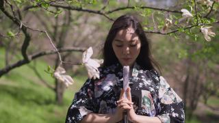 年轻自信的亚洲美女正面肖像，手握扇子看着相机。美丽的日本女士在春天的公园里与盛开的树木合影。缓慢的运动。视频素材模板下载