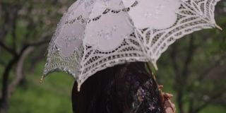 侧视人像华丽自信的亚洲女性手持白色太阳伞慢动作转身。轻松积极的美丽小姐在阳光明媚的夏日公园户外休息，休闲概念。