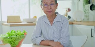 家中厨房里一位年长妇女微笑着看着相机。坚强年迈的老祖母戴着眼镜，在家里感到幸福和享受退休生活。保健和医疗观念。