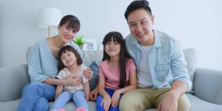 亚洲幸福家庭的肖像花时间与孩子一起在家里。年轻可爱的小女孩和父母坐在沙发上微笑着，看着摄像机在客厅里。活动关系的概念