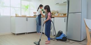亚洲漂亮的母亲教小女孩打扫厨房在家里。爱美丽的父母妈妈帮助和支持小女儿在家打扫房间的地板。活动关系的概念。