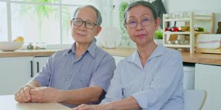 老夫妇在家里的厨房微笑着看着相机的照片。健硕年迈的男女祖父母戴着眼镜，在家中享受退休生活。保健和医疗观念。