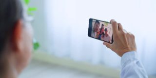 亚洲老年妇女与家人远程视频通话的特写。在家里的客厅里，年迈的爷爷拿着手机与年轻的夫妇和孙子孙女们进行虚拟在线聊天。