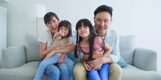 亚洲幸福家庭的肖像花时间与孩子一起在家里。年轻可爱的小女孩和父母坐在沙发上微笑着，看着摄像机在客厅里。活动关系的概念